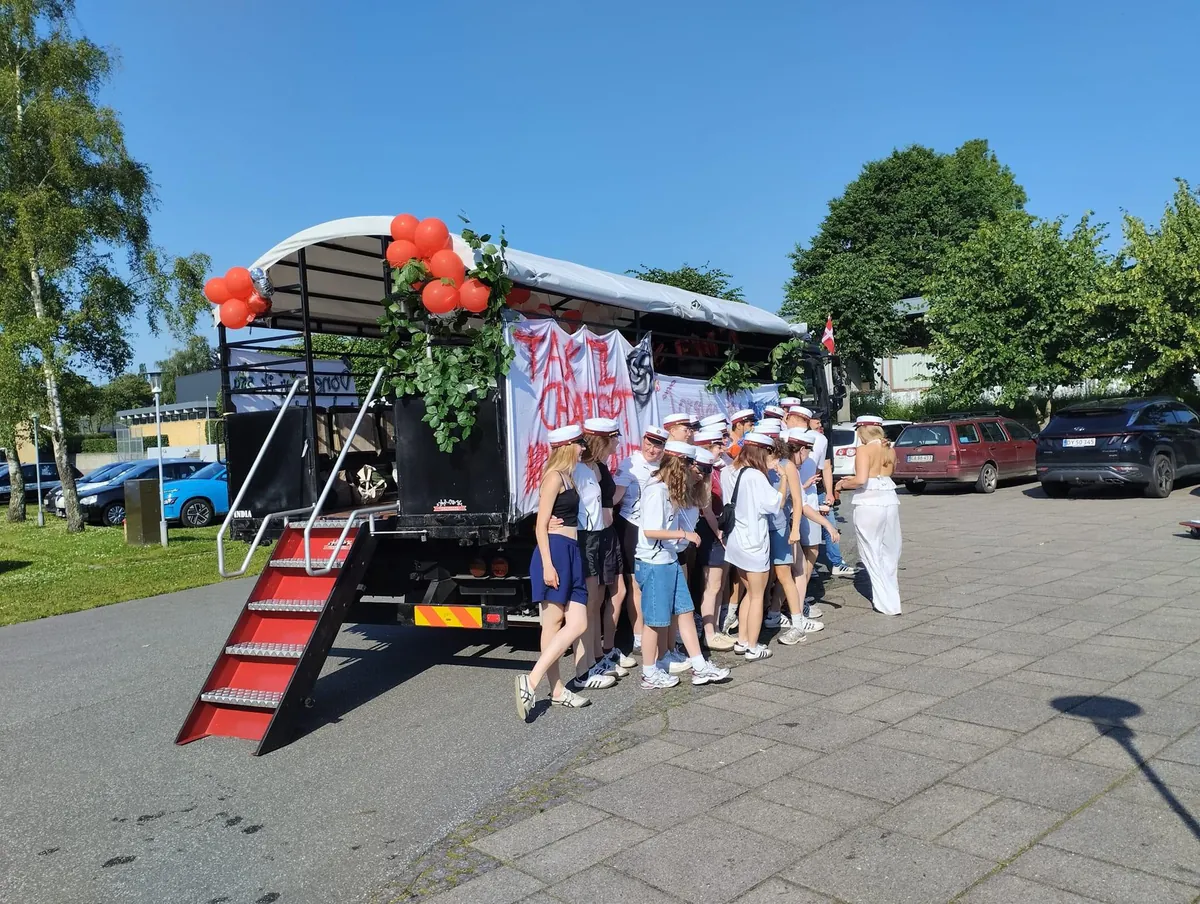 Studenter med huer foran en af EventTrucks’ studentervogne med røde balloner, grønne grene og hjemmelavede bannere i Aarhus